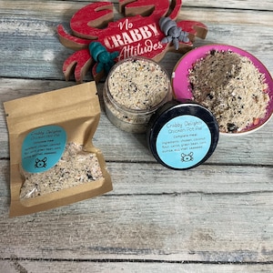 May include: An assortment of pet food products, including a small bag, a jar, and a container of "Crabby Delights Chicken Pot Pie" complete meal. The products are on a wooden surface, with a red crab decoration and the text "No Crabby Attitudes".