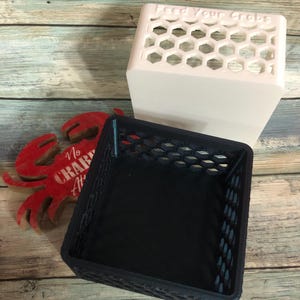 May include: A white, honeycomb-patterned container with the text "Feed Your Crabs" sits above a dark blue, honeycomb-patterned basket. A red crab-shaped decoration with the text "No Crab Allowed" is also present.
