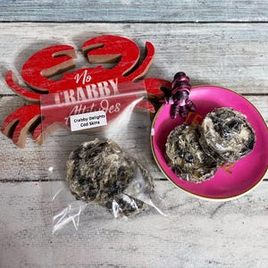 May include: A wooden red crab decoration with the text "No Crabby Ht Jes" and a clear bag of "Crabby Delights Cod Skins". Two cod skins are on a pink plate with a small purple octopus figurine.