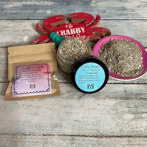 May include: An assortment of "Crabby Delights" bunny food products. The image shows a small brown paper bag, a clear jar, a small black container, and a pink dish, all containing a mix of ingredients. A red crab-shaped decoration is in the background.