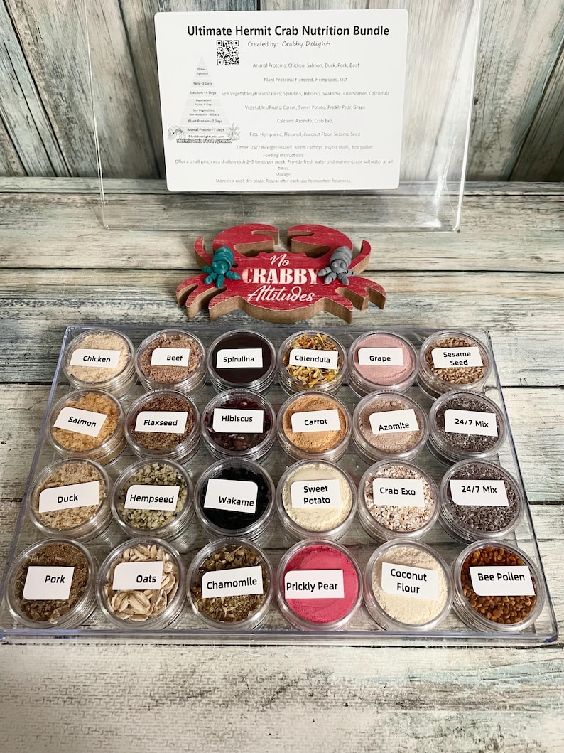 May include: A clear plastic tray filled with small, labeled containers of hermit crab nutrition. The labels include "Chicken," "Beef," "Spirulina," and more. A red crab-shaped decoration with the text "No Crabby Attitudes" sits above the tray.
