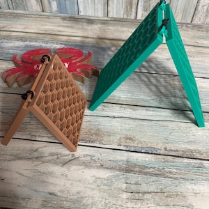 May include: Two foldable, triangular stands featuring a textured honeycomb pattern on their surfaces. One stand is light brown, and the other is teal. Both are constructed from two hinged panels connected by small black fasteners at the top corners.