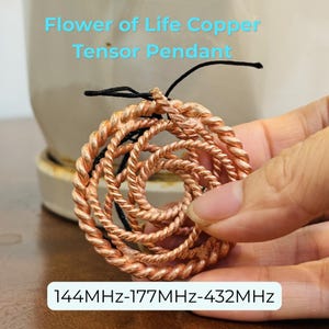 May include: A copper tensor pendant in a flower of life design. The pendant is made of twisted copper wire and has a circular shape. The text on the image reads "Flower of Life Copper Tensor Pendant" and "144MHz-177MHz-432MHz".