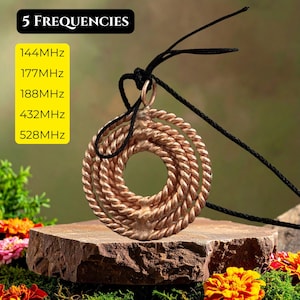 May include: A copper-colored pendant necklace with a circular design, featuring three concentric coils. The necklace hangs from a black cord. The image includes text that reads "5 FREQUENCIES" and lists frequencies in MHz.