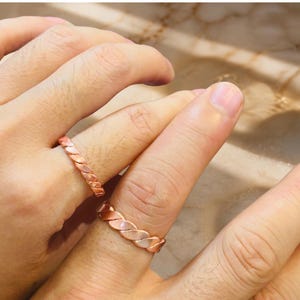 May include: Two copper-colored rings featuring a twisted, braided metal design. The rings have a polished, metallic finish with a repeating diagonal pattern that wraps around the entire circumference of each band, creating a textured appearance.