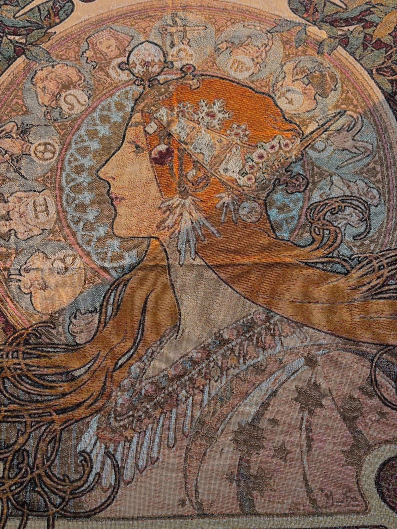 May include: A tapestry featuring a woman in profile with long auburn hair and an elaborate headdress. The artwork has a vintage aesthetic, with a circular design behind the woman's head and intricate floral and geometric patterns. The color palette includes warm tones of orange, beige, and brown.