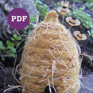 Peut inclure: Un objet artisanal en forme de ruche de couleur beige avec des brins de paille, accompagné de trois épingles décoratives en forme d'abeille. Une épingle à abeille porte une couronne dorée. L'image comprend le texte "PDF" dans un cercle violet.