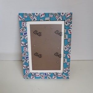 May include: Rectangular photo frame with a blue fabric border patterned with white and red Mahjong tiles. The frame has a white inner border and a brown backing with metal fasteners.