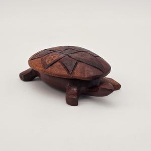 May include: A handcrafted wooden turtle figurine with a detailed shell design. The turtle is made of dark brown wood and has a smooth finish. The figurine is a decorative item.