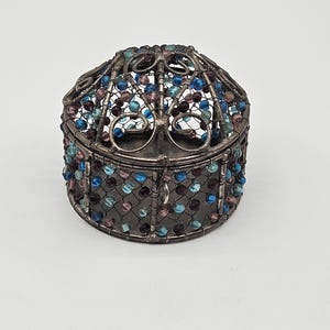 May include: A round, cage-like container crafted from dark silver-toned metal wire. The structure features a domed top and cylindrical sides, intricately woven with small, translucent beads in shades of deep blue, light blue, and purple.