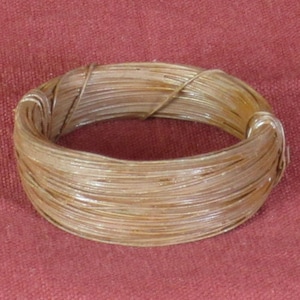 May include: A coiled, circular object made of thin, light brown strands. The strands are tightly wound together, forming a solid ring. The object appears to be made of a natural material, possibly fiber or plant-based.