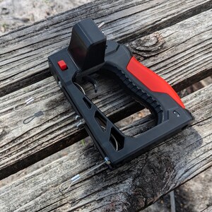 Puede incluir: Un transmisor de control remoto negro y rojo con un gatillo y un bot&oacute;n rojo. El mango es rojo y el cuerpo es negro. Se ven dos cables plateados con bucles.