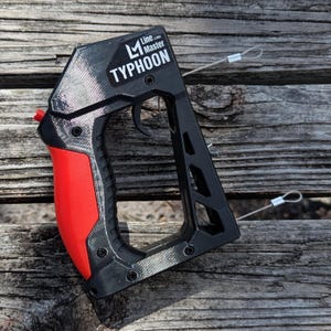 Puede incluir: Una herramienta Line Master Typhoon negra y roja con un gatillo y dos cables met&aacute;licos. La palabra "TYPHOON" est&aacute; impresa en la herramienta. La herramienta est&aacute; sobre una superficie de madera.