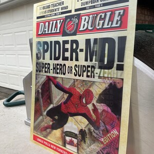 May include: A vintage-style Daily Bugle newspaper print featuring Spider-Man. The headline reads "SPIDER-MD! SUPER-HERO OR SUPER-ZERO?" with additional text about crime and local news. The image showcases Spider-Man in action, with a distressed, aged aesthetic.