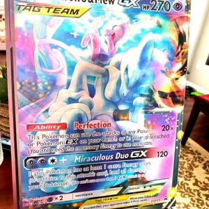 May include: A framed Pokémon trading card featuring Mewtwo & Mew GX. The card has a colorful design with the text "Mewtwo & Mew GX" and "TAG TEAM". The card's HP is 270.