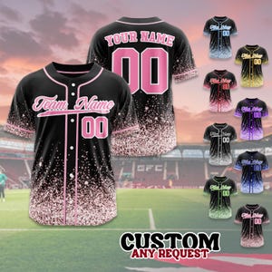 May include: Black baseball jersey with pink accents and a glitter effect. The front features "Team Name" and the number "00". The back displays "YOUR NAME" and "00". Additional jerseys in various colors are shown. Text at the bottom reads "CUSTOM ANY REQUEST".