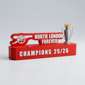 Może przedstawiać: Czerwony element dekoracyjny z białym napisem "NORTH LONDON FOREVER" i "CHAMPIONS 25/26". Zawiera emblemat armaty i srebrne trofeum ze złotą koroną. Prawdopodobnie przedmiot kolekcjonerski o tematyce sportowej.