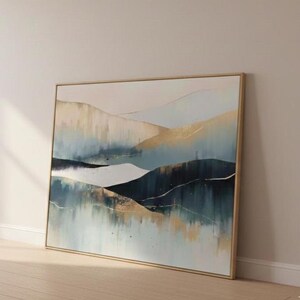 May include: Abstract landscape painting with a gold frame. The artwork features a mountain range in shades of blue, gold, and white. The painting is leaning against a wall in a room with natural light.