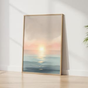 Può includere: Una stampa artistica incorniciata raffigurante un sereno tramonto sull'oceano. L'opera presenta un gradiente di colori, con un sole giallo brillante che si riflette sull'acqua, passando a tonalità rosa e blu. La stampa è esposta su un pavimento in legno.