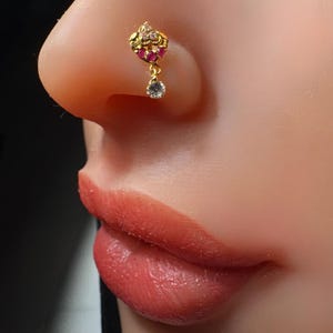Peut inclure: Bague de nez en or avec un pendentif. Le pendentif est décoré de pierres roses et blanches.