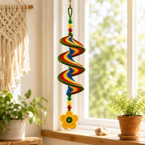 May include: A hanging spiral decoration made of crocheted yarn in vibrant red, yellow, blue, and green stripes. The spiral features a loop at the top and a yellow crocheted flower at the bottom, accented with small red, yellow, and green beads.