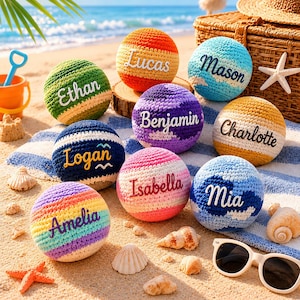 Puede incluir: Una colección de bolas de ganchillo coloridas con nombres bordados como "Ethan", "Lucas", "Mason" y "Benjamin". Las bolas están dispuestas en una playa de arena, junto con conchas marinas y gafas de sol, creando una escena veraniega.