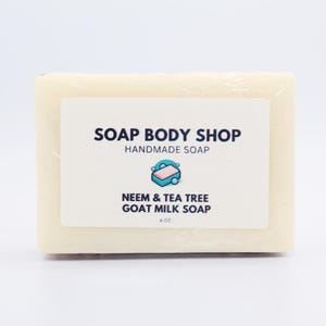 Op de afbeelding: Een witte zeep met een label waarop staat "SOAP BODY SHOP HANDMADE SOAP NEEM & TEA TREE GOAT MILK SOAP 4 OZ"