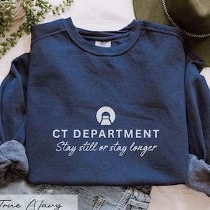 May include: A navy blue sweatshirt with the text "CT DEPARTMENT" and the phrase "Stay still or stay longer" in white. The sweatshirt has a crew neck and long sleeves. The words "True Navy" are at the bottom.