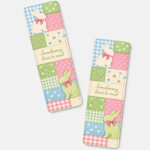 Puede incluir: Dos marcapáginas decorativos con un diseño de patchwork. Cada marcapáginas presenta un conejito blanco con un lazo rosa, un conejito verde con un lazo rosa y el texto "Somebunny loves to read". Los marcapáginas tienen una combinación de colores pastel.
