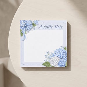 May include: A square notepad with a light blue border and the text "A Little Note". The notepad is decorated with watercolor-style blue and white hydrangea flowers and green leaves in the corners.