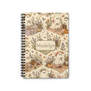 May include: A spiral-bound notebook with a cream-colored cover featuring a repeating pattern of ghosts having picnics with flowers, butterflies, pumpkins, and baskets. A central rectangular label displays the name Madelyn in brown text.