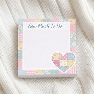 May include: A square notepad with a patchwork design in pastel colors. The notepad features the text "Sew Much To Do" and a heart-shaped patch. The background is a white, textured surface.