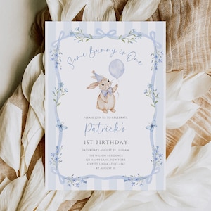 Peut inclure: Carte d'invitation bleu clair et blanche avec le texte "Some Bunny is One" et "Patrick's 1st Birthday". Elle présente une illustration à l'aquarelle d'un lapin tenant un ballon, entourée d'éléments floraux et de rubans.