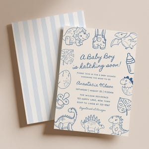 May include: Baby shower invitation with a light beige background and blue dinosaur illustrations. The text "A Baby Boy is hatching soon!" is featured, along with event details. The back of the invitation has a light blue and white striped pattern.