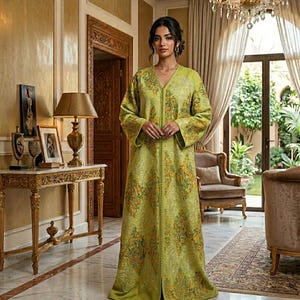 May include: A woman wearing a long, light green dress with intricate yellow and orange floral embroidery. The dress has long sleeves and a V-neck. The background features a luxurious interior with a chandelier and ornate furniture.