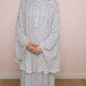 May include: A white and blue floral prayer outfit, including a head covering and a matching skirt. The outfit is made of a lightweight fabric and is worn by a person. The floral pattern is small and delicate, covering the entire outfit.