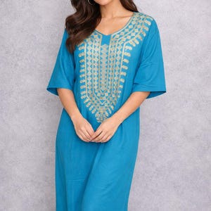 May include: A long, turquoise dress with short sleeves and a V-neckline. The dress features intricate gold embroidery around the neckline and down the center. The fabric appears soft and flowing, suitable for warm weather.