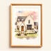 May include: A watercolour painting of a house with a light stone exterior, dark roof, and a wooden door. The artwork is framed in a light wood frame. The sky has pink, orange, and blue hues.