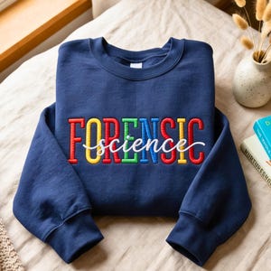 May include: A navy blue sweatshirt with the words "FORENSIC science" embroidered in colorful thread. The word "FORENSIC" is in bold, block letters, with each letter a different color. The word "science" is in a cursive font.