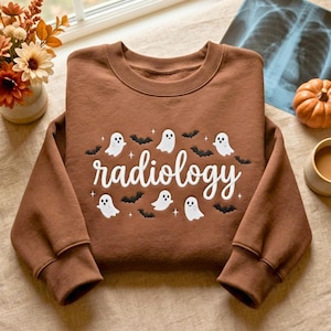 May include: A brown crewneck sweatshirt featuring white embroidered text that reads radiology, surrounded by small white ghost figures, black bat silhouettes, and tiny star accents across the center of the chest area.