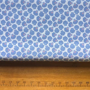 May include: A fabric with a repeating pattern of blue seashells on a white background. Each shell has a pink center. The fabric is likely cotton or a similar material, suitable for sewing projects or home decor.