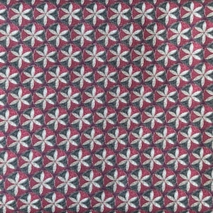 May include: A close-up of a patterned fabric with a repeating floral design. The pattern features white, grey, and burgundy flower-like shapes arranged in a grid. The fabric has a textured appearance.
