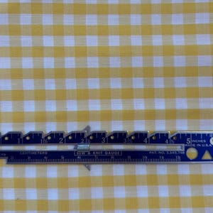 May include: A close-up of a yellow and white gingham fabric with a ruler measuring 12.7 cm. The ruler is blue and silver with black markings.