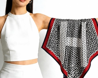May include: A square scarf featuring a repeating black and white geometric pattern of small triangles. The scarf is bordered by a thick red stripe followed by a thin navy blue edge, creating a distinct frame around the central graphic design.