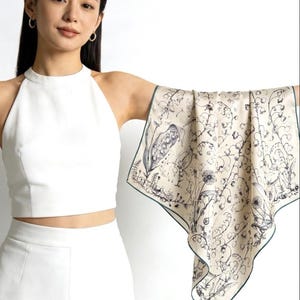 May include: A square scarf featuring a cream-coloured background with a detailed black line art botanical print of various flowers and plants. The scarf has a thin dark green border along its edges and a smooth, lightweight fabric texture.