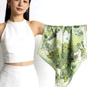 May include: A square silk scarf featuring a detailed forest scene with various shades of green trees, foliage, and small illustrated animals. The scarf has a light green border and a white background, showcasing a repeating nature-inspired pattern.