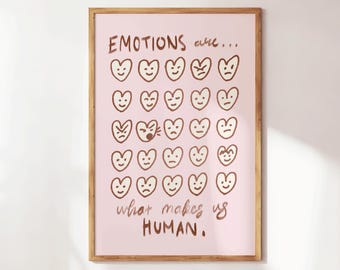Może przedstawiać: Oprawiony wydruk artystyczny z jasnoróżowym tłem i drewnianą ramą. Wydruk zawiera słowa "EMOTIONS are... what makes us HUMAN." w brązowym skrypcie. Brązowe twarze w kształcie serca z różnymi wyrazami twarzy są ułożone w rzędach.