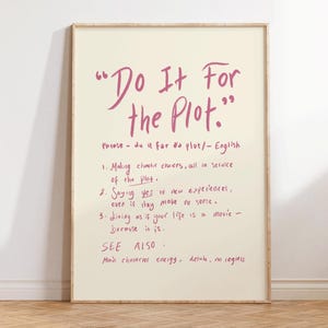 Könnte beinhalten: Ein gerahmtes Poster mit dem Satz "Do It For the Plot" in rosa Schrift. Das Poster enthält eine Definition und drei Punkte zum Satz. Das Poster befindet sich in einem hellbeigen Rahmen und lehnt an einer Wand.