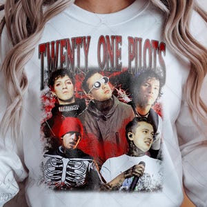 Może przedstawiać: Biała bluza z grafiką zespołu Twenty One Pilots na czerwono-czarnym tle. Projekt ma charakter vintage, z nazwą zespołu w czerwonych literach u góry.