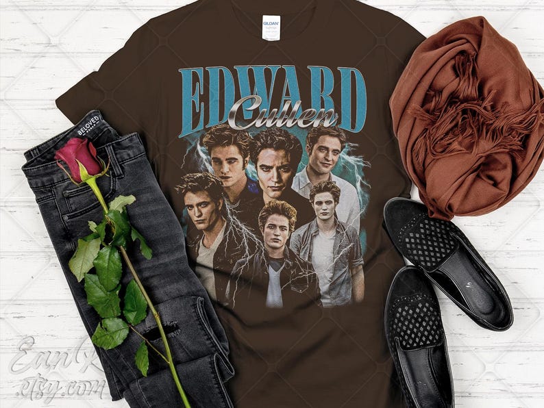 May include: Brown t-shirt featuring a graphic of Edward Cullen with the text "EDWARD Cullen" in blue and silver. The shirt is styled with black jeans, a rose, a brown scarf, and black loafers.